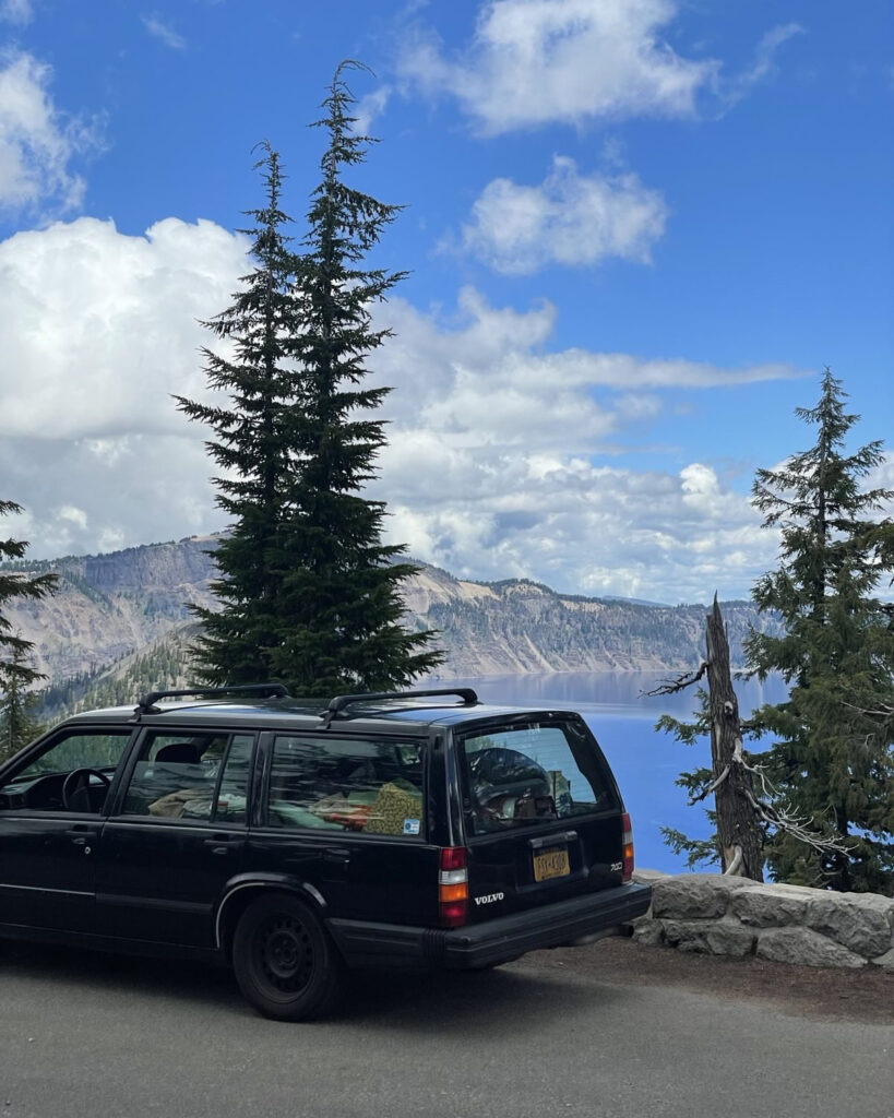 An old Volvo car with a lake and mountains in the background